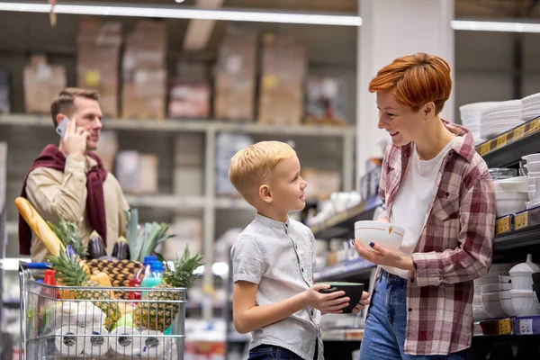 Πλάγια άποψη για μικρό παιδί αγόρι ζητήσει από τη μητέρα να αγοράσει όμορφα πιάτα στο κατάστημα — Φωτογραφία Αρχείου