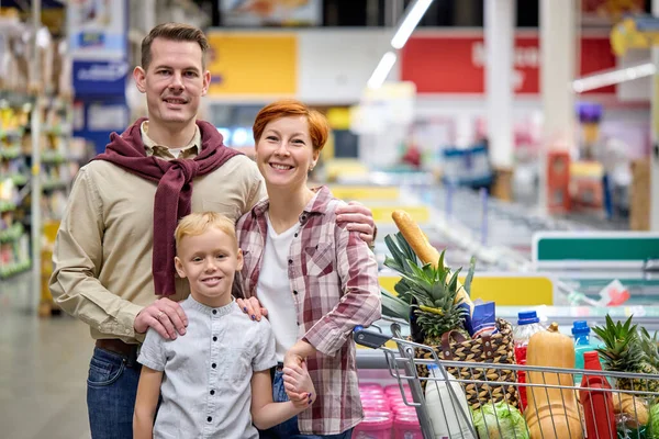 Retrato de jovem família agradável com o filho olhando para câmera posando, durante as compras — Fotografia de Stock