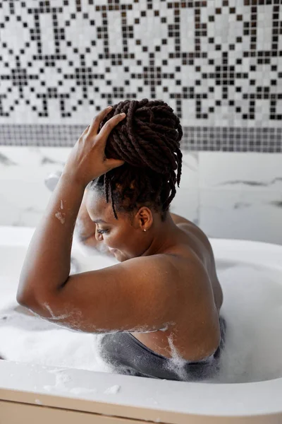 Расслабленная африканская женщина, лежащая на ванне, наслаждаясь временем в одиночестве по выходным, концепция гигиены — стоковое фото
