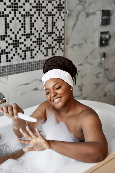 Портрет африканской американки, делающей маникюр во время купания в спа дома — стоковое фото