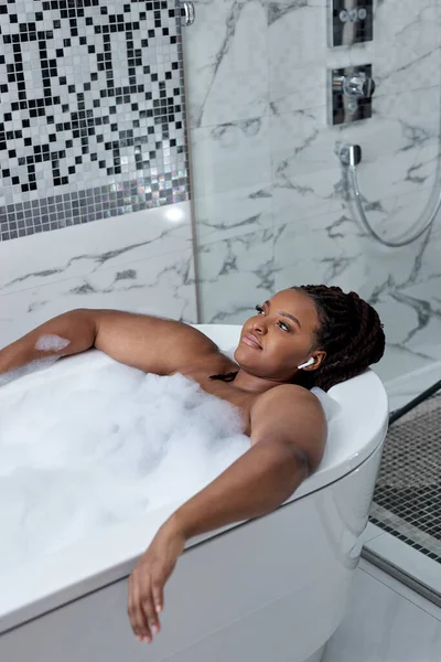 Relaxado mulher africana tomando banho com espuma com prazer, desfrutando de spa, higiene — Fotografia de Stock