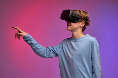 Genç bir çocuk, VR kulaklığı deniyor ve renkli arka planda başka bir dünyayı keşfediyor.