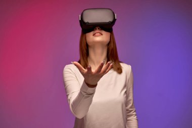 Sanal gerçeklik kaskı takmış, VR gözlükleri ekranına bakan heyecanlı genç bir kadın.