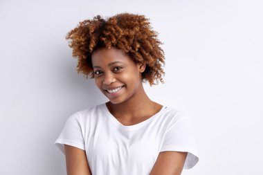 Kıvırcık saçlı, kameraya bakan sevimli Afro-Amerikan bayan.