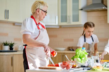 Önlüklü büyükanne, yaşlı bayan pizza yaptığı için domates doğrayacak.