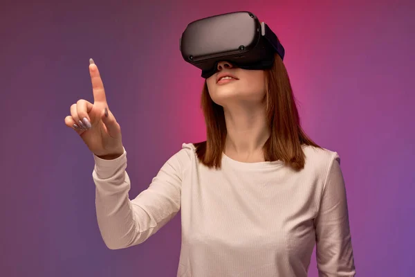Radostná mladá žena v helmě virtuální reality, dívá se do VR brýle obrazovky — Stock fotografie
