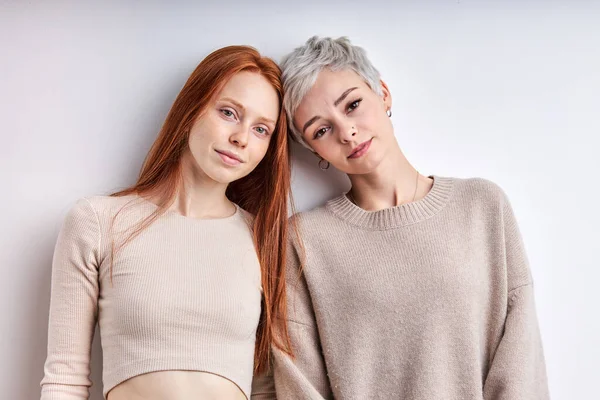 Two friendly caucasian girlfriends in beige casual shirt posing looking at camera, feel calmness — Stock Photo, Image