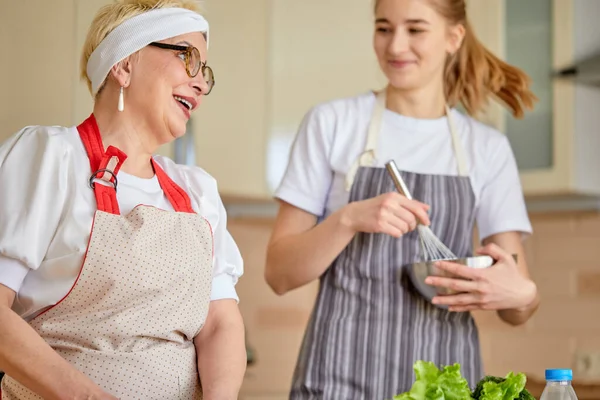 둘 이 더 재밌어. 손녀딸 과 함께 앞치마를 두르고 요리를 하고 있는 행복 한 성숙 한 여인 — 스톡 사진