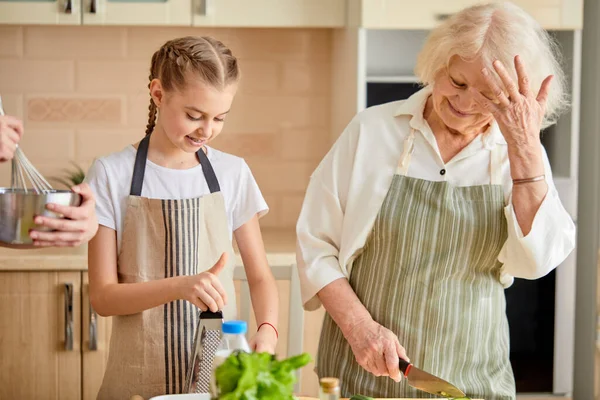 Mais engraçados juntos. Mulher idosa feliz em um avental cozinhar em conjunto com neta — Fotografia de Stock