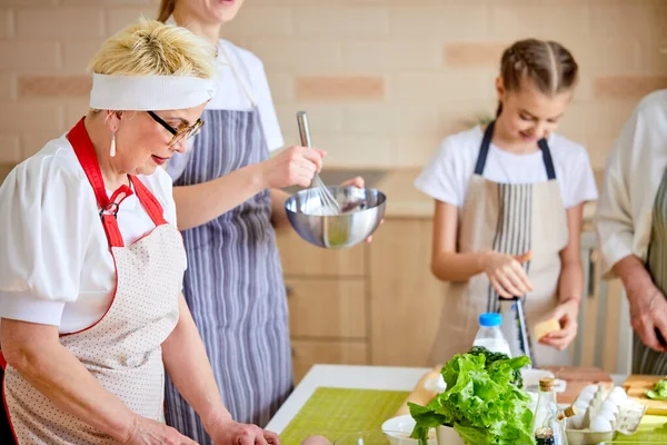 Vista lateral de la abuela elegante mujer mayor en delantal de cocina con los niños nietas en la cocina — Foto de Stock