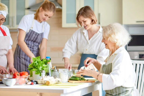 Side view on happy senior woman cooking with family, chopping fresh vegetables