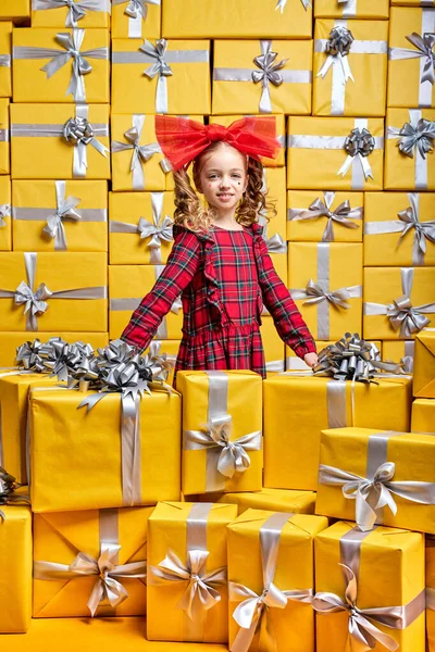 Diligente niña caucásica en vestido rojo a cuadros entre muchos regalos. Día Internacional de la Mujer cumpleaños, concepto de vacaciones — Foto de Stock