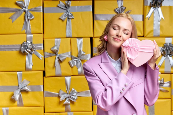 Mujer caucásica soñadora posando en un estudio rodeado de cajas de regalo celebrando cumpleaños, regocijando muchos regalos — Foto de Stock