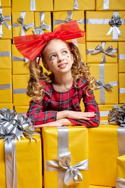 Niña soñadora en fiesta a cuadros llevar sonriendo, buscando animado al lado de las cajas llenas de regalos — Foto de Stock