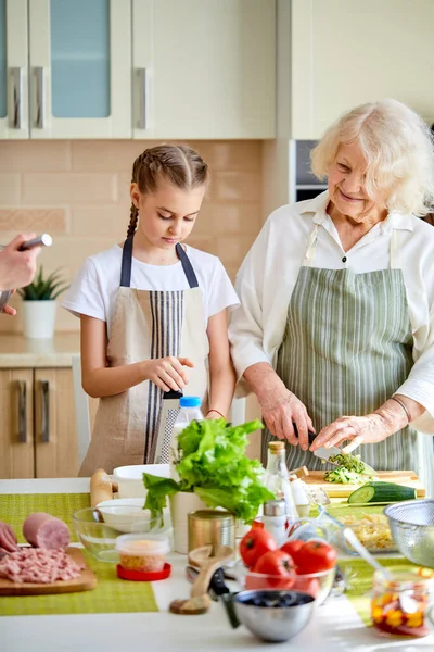 Ευτυχισμένη ενήλικη ηλικιωμένη κυρία που μαθαίνει στην έφηβη πώς να μαγειρεύει υγιεινά φαγητά. — Φωτογραφία Αρχείου