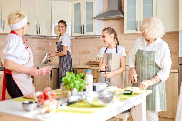 Θετική έφηβη πλένει τα πιάτα, ενώ άλλοι ετοιμάζουν φαγητό στο τραπέζι. — Φωτογραφία Αρχείου