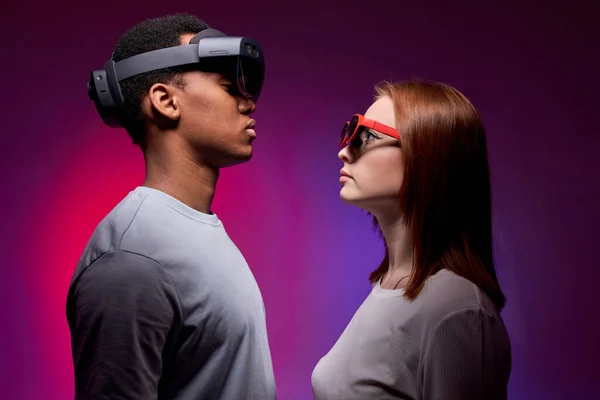 Couple in casual clothes stand with VR helmets and play games in virtual reality