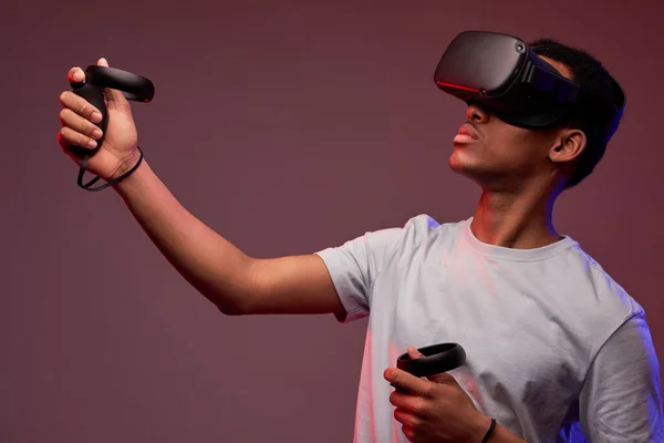 Jeune afro gars jouer à des jeux VR en réalité virtuelle casques sur fond lumineux coloré — Photo