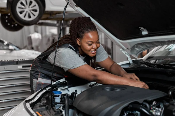 Молода чорношкіра працівник по ремонту автомобілів перевіряє рівень мастила в двигуні автомобіля, вид збоку — стокове фото