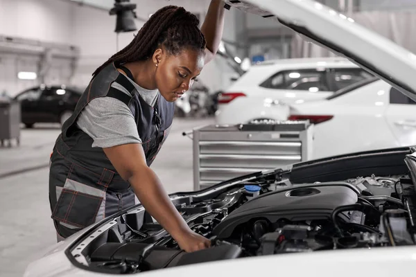 Afrikaanse auto monteur vrouw is het onderzoek onder kap van de auto bij reparatie garage — Stockfoto