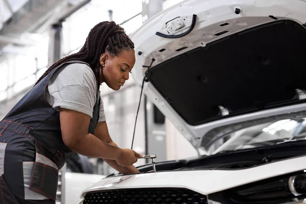 Zwarte vrouwelijke monteur holding moersleutel controle op de motor van de auto, voor reparatie en controle — Stockfoto