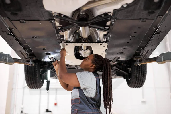 Black female auto mechanic fixing car, mechanic repairing car on lift in garage