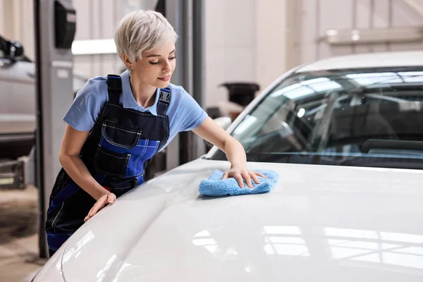 Korte haren blonde vrouw polijsten de witte auto kap met blauwe doek na het wassen — Stockfoto