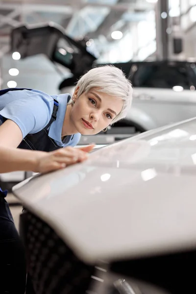 Kvinnlig auto mekaniker vidrör ytan av målade och rena bilkaross i bilverkstad — Stockfoto