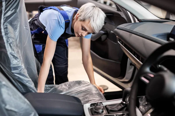 Женщина автомеханик покрывает полиэтилен на автомобильном сидении, чтобы он не испачкался — стоковое фото