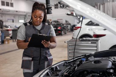 Afro kadın makine mühendisi kontrol listesi kağıtlarını tutuyor ve panoya not alıyor
