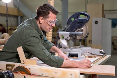 Ahşap işçiliği için koruyucu gözlük takan yeşil gömlekli genç bir marangoz.