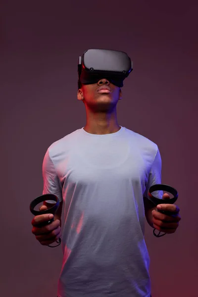 Jeune afro gars jouer à des jeux VR en réalité virtuelle casques sur fond lumineux coloré — Photo