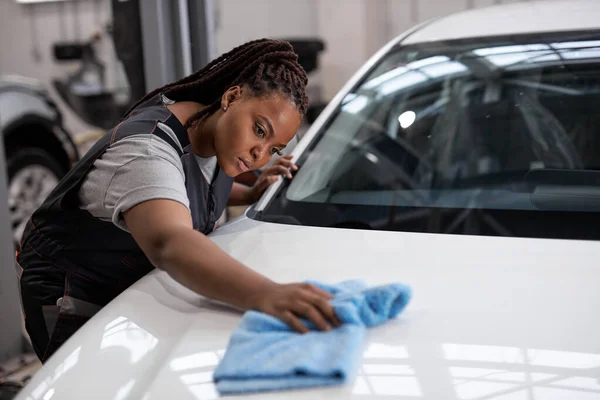 Serieuze vrouw houdt blauwe microvezel in de hand en poetst de auto. Reiniging wassen auto — Stockfoto