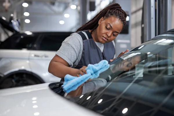 Confident Female afro auto mechanic cleaner is cleaning car window glass with rag