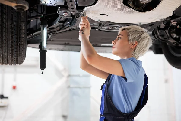 Жінка-автомеханік фіксує машину, ремонтує машину на ліфті в гаражі. вид збоку — стокове фото