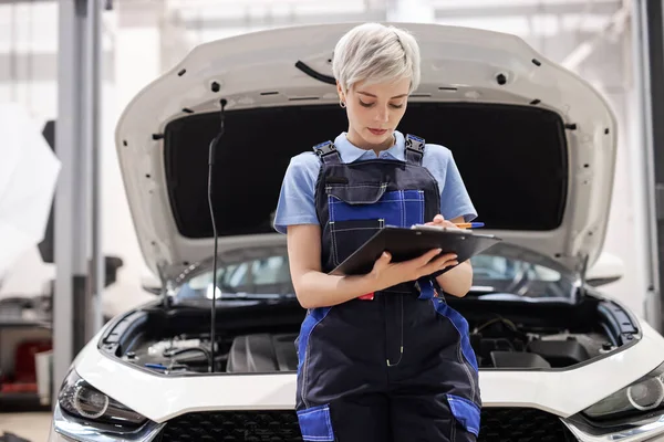 Auto reparatieservice, vrouwelijke automonteur controleren automotor, schrijven checklist op klembord — Stockfoto