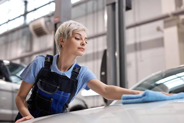 Короткошерста блондинка полірує білий автомобільний капюшон з синьою ганчіркою після прання — стокове фото