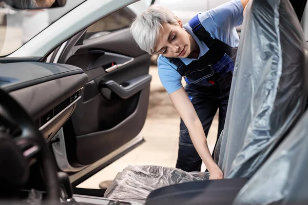 Vrouwelijke auto monteur dekt polyethyleen op autostoel, zodat het niet vies — Stockfoto