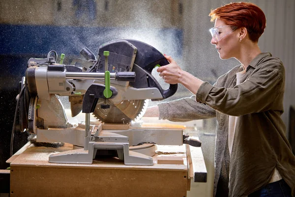 Vista lateral no carpinteiro fêmea confiante usando máquina elétrica, desfrutar de trabalhar madeira — Fotografia de Stock