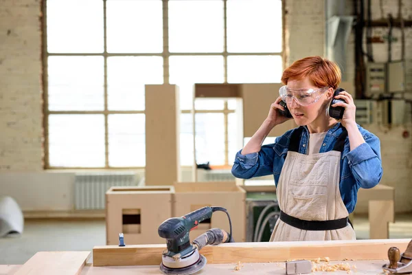 woman carpenter wearing headset before woodworking, cutting wood using power saw