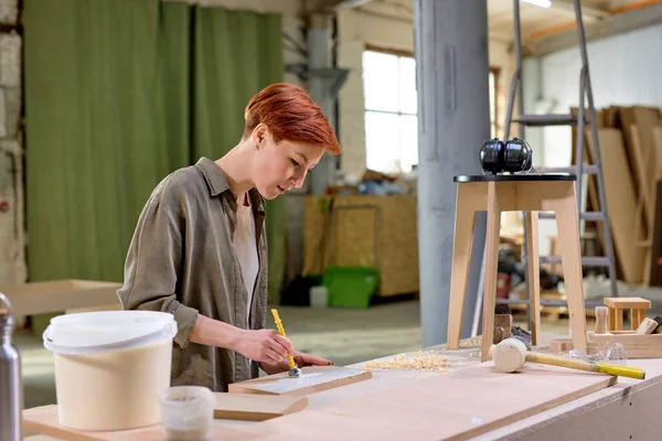Mulher de carpinteiro pinta a ripa de madeira da produção da mobília na mesa na oficina — Fotografia de Stock