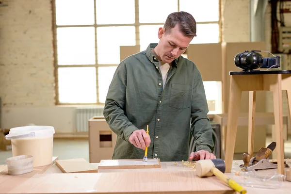 Artisanat en bois, homme artisan charpentier peinture avec brossele panneau en bois, vue de côté — Photo