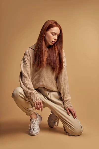 Gyönyörű fiatal nő modell divatos ruhában ül a padlón elszigetelt bézs — Stock Fotó