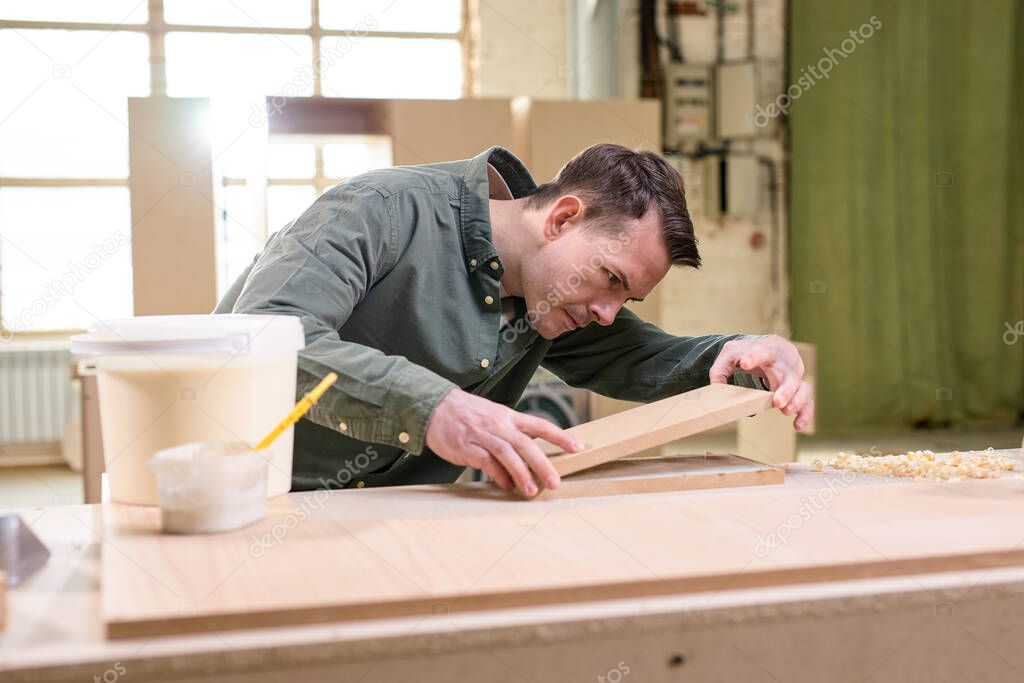 male joiner comparing the length and width of wooden material while woodworking