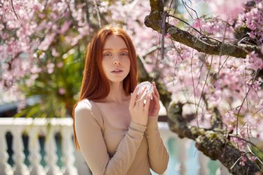 Güneşli bir günde botanik bahçesinde krem ve güzellik ürünleri kullanan bir kadın.