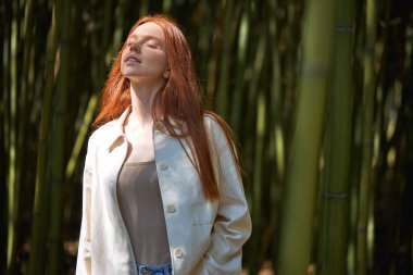 Günlük kıyafetlerle poz veren kadın model. Güneşin altında, bambu ağaçlarının arasında rahat bir kadın..