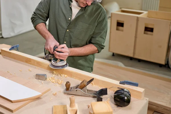 Carpinteiro macho cortado cuidadosamente alisando material de madeira com lixadeira elétrica — Fotografia de Stock