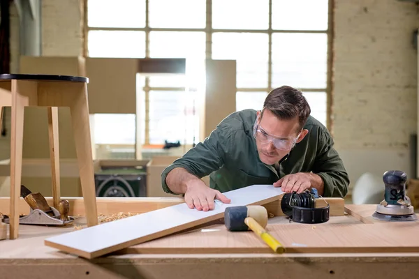 Marceneiro profissional comparando, verificando o comprimento e a superfície do material de madeira — Fotografia de Stock