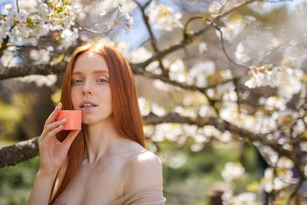 Fêmea de boa aparência usando creme hidratante posando no jardim da primavera com árvores florescendo — Fotografia de Stock