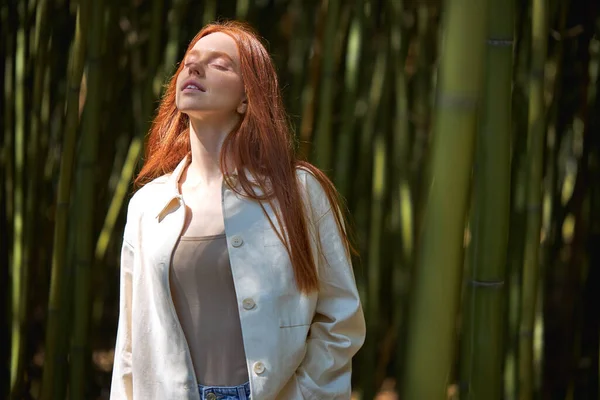 Modelo feminino posando em desgaste casual. Mulher relaxada entre árvores de bambu sob a luz do sol. — Fotografia de Stock